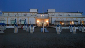 Un hôtel en bord de mer doté de nombreux balcons, d’un espace extérieur aménagé et d’une zone sablonneuse avec des chaises longues.
