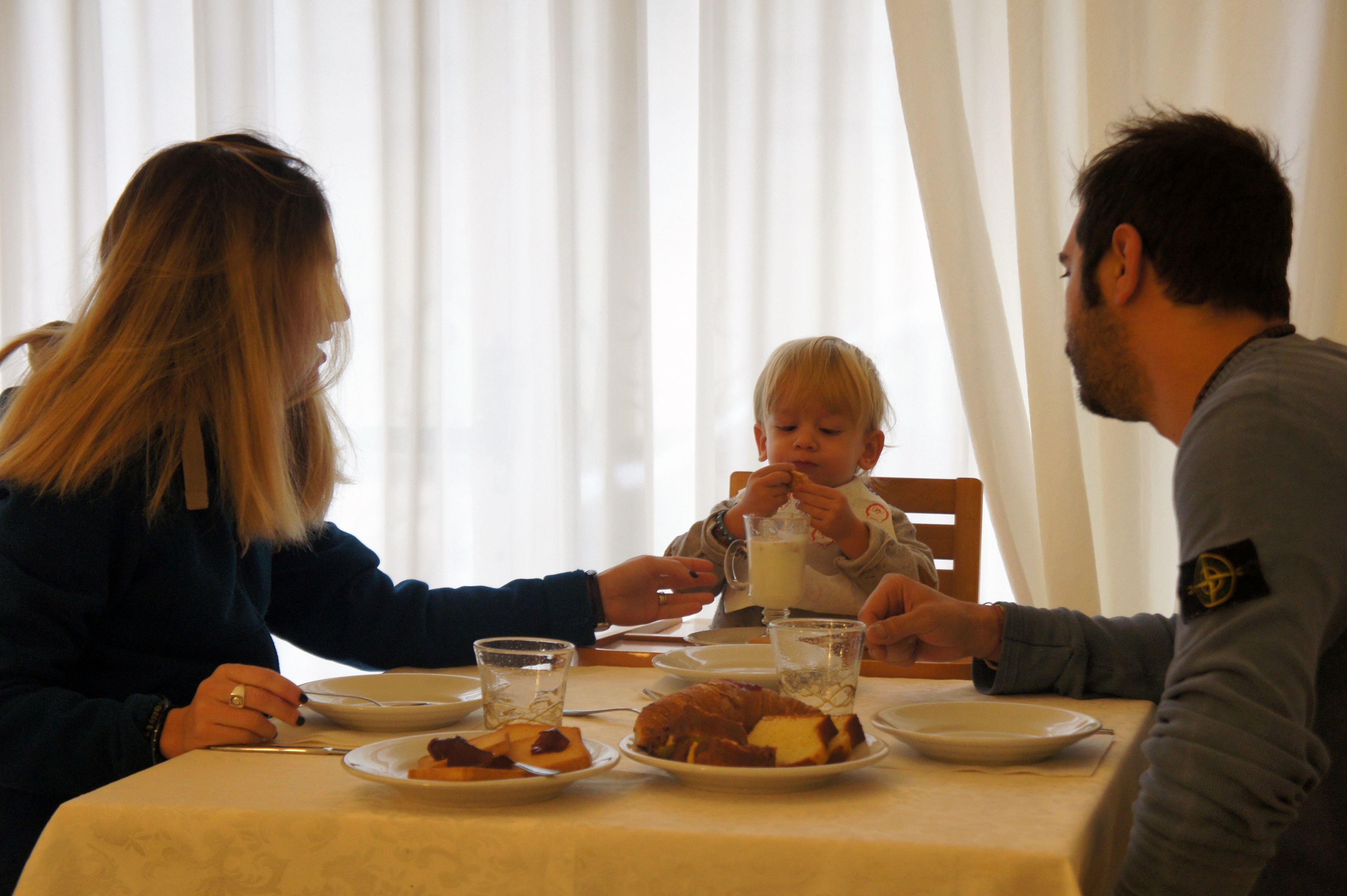 Une famille est assise à table, devant des assiettes remplies de nourriture et des boissons.