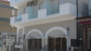 Hotel de varios pisos con balcones, entrada cubierta y un letrero que indica una zona de estacionamiento.