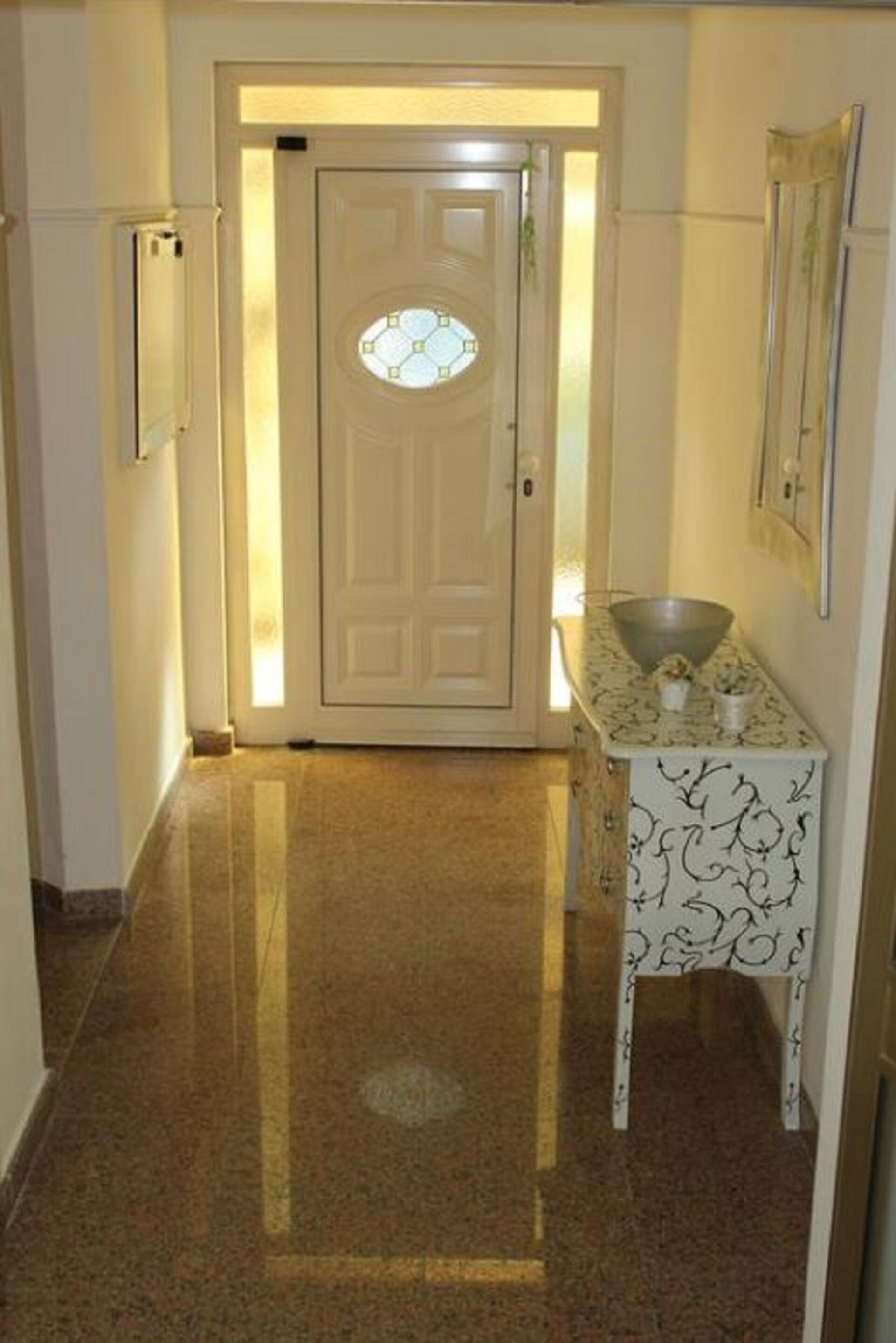Un pasillo con una puerta, una mesita con un cuenco y un espejo en la pared.