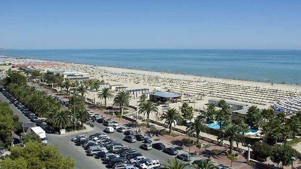 Un complejo turístico en la playa con filas de sillas, un estacionamiento y palmeras.