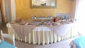 Una mesa de buffet con diversos alimentos y utensilios, ubicada en un salón con una pared amarilla y un espejo encima.