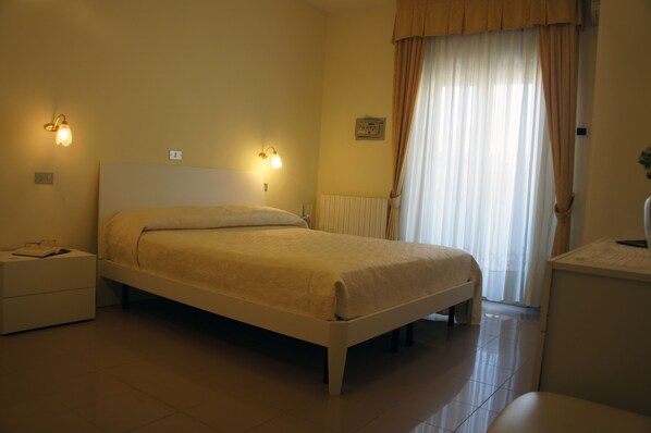 A bedroom with a bed, bedside tables, and a window with curtains. - Hotel Solaris (Giulianova)