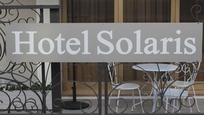 Señal de Hotel Solaris con valla de hierro forjado y sillas blancas al frente.