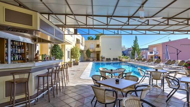 An outdoor pool area with lounge chairs and tables, a bar with bottles, and a staircase leading to an upper level.