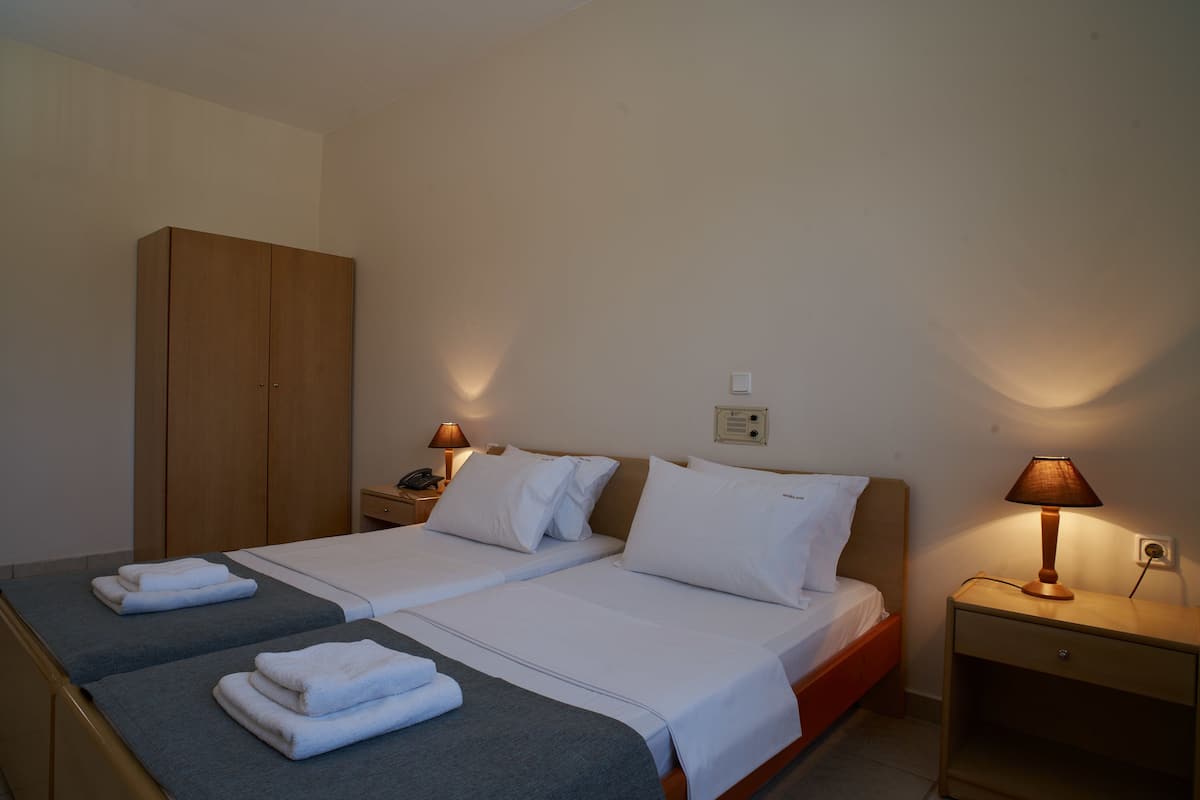 Une chambre d’hôtel avec deux lits, une armoire, des lampes de chevet et des serviettes soigneusement pliées.