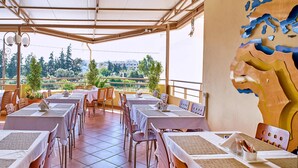A restaurant with outdoor seating, tables covered with white tablecloths, and a view of the surrounding landscape.