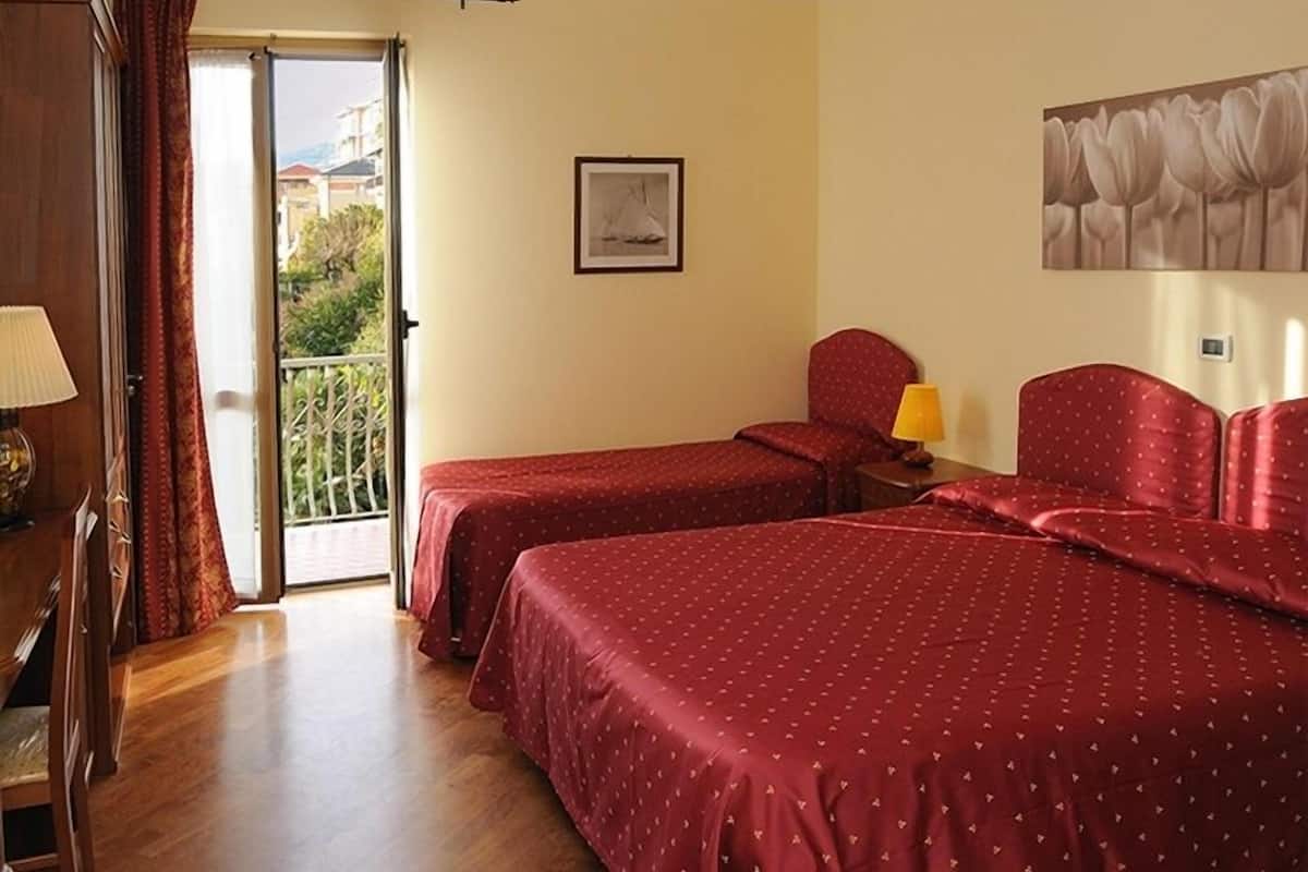 Une chambre d’hôtel avec deux lits, un balcon, un bureau avec une lampe et un tableau au mur.