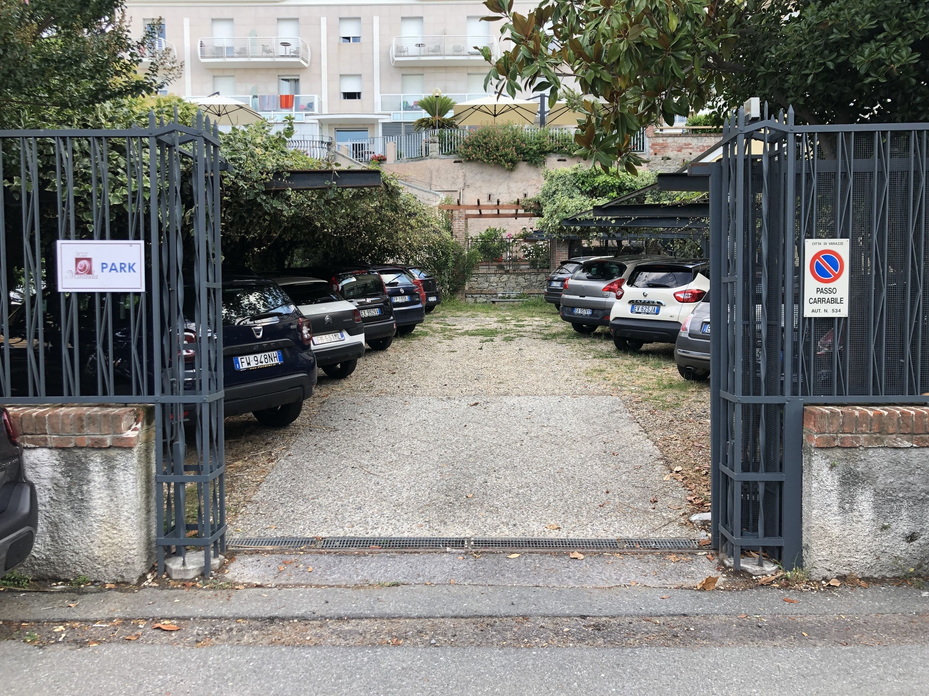 A gated parking area with multiple cars parked in rows, a sign indicating a park, and a no parking sign.