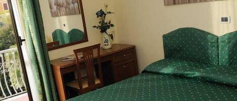 A bedroom with a bed, a desk, a chair, a dresser, a vase with flowers, and a window with curtains.
