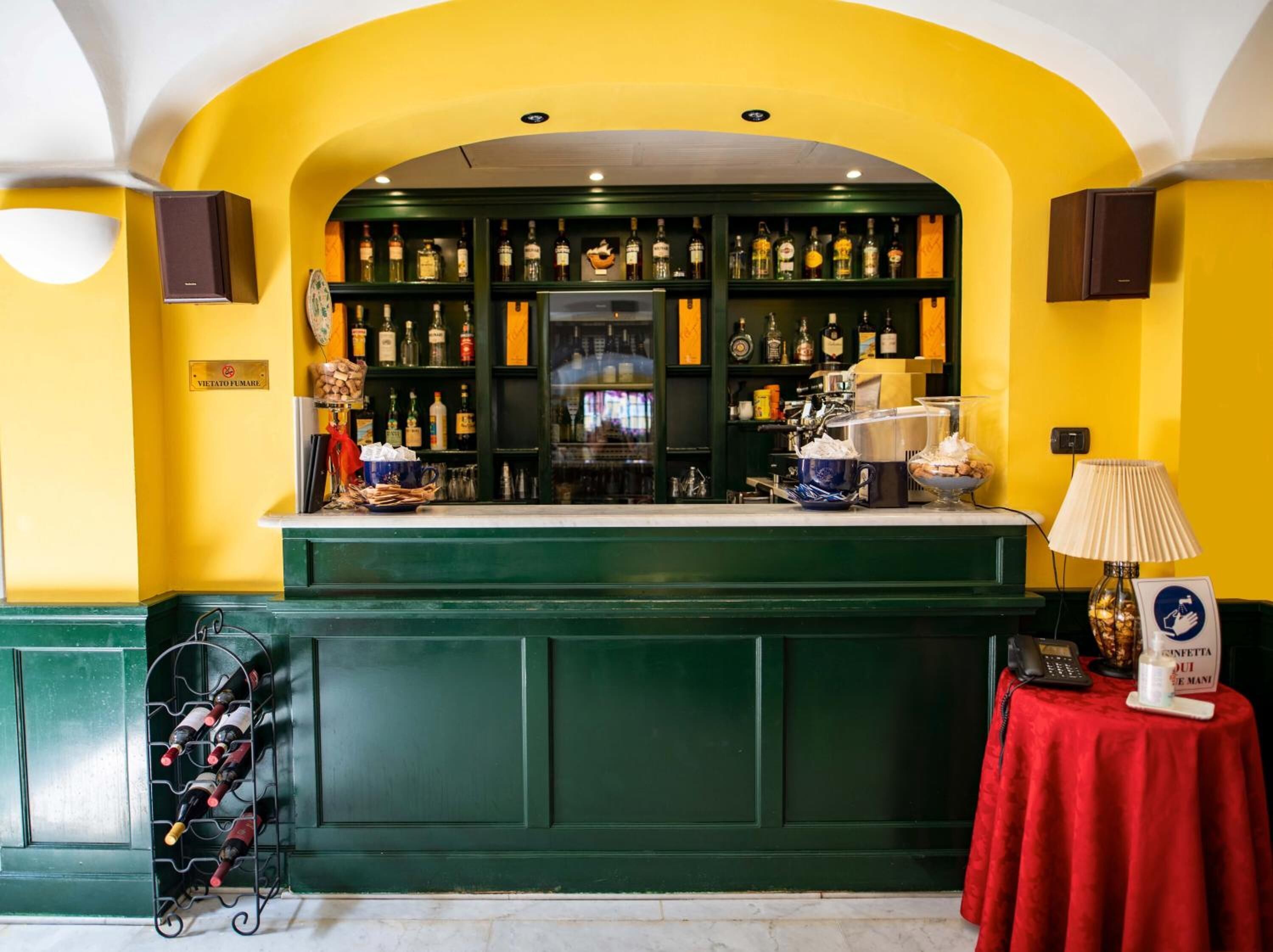 Een bar met een groen aanrecht, flessenkasten vol drank en een rode tafel met een bord.