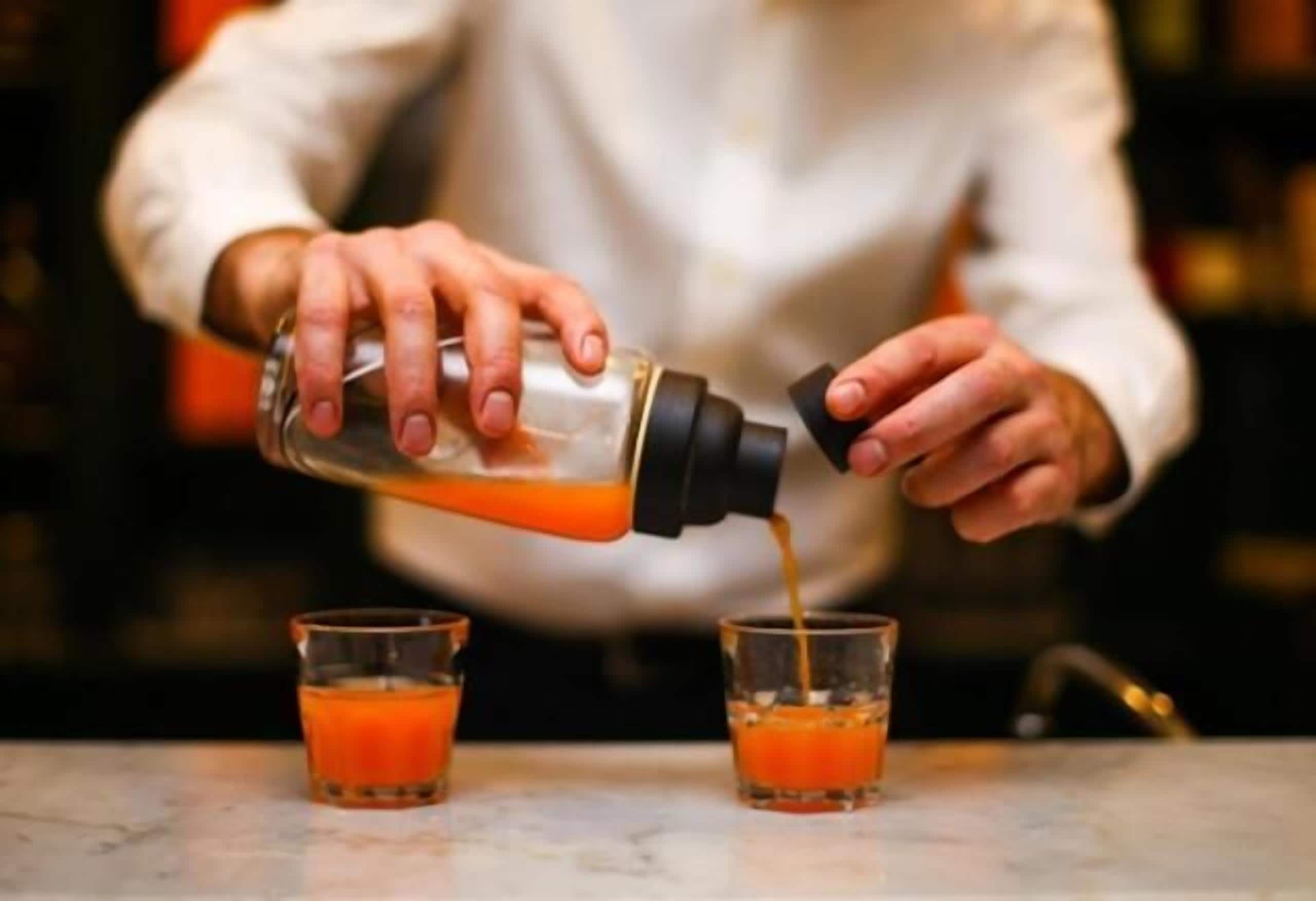 A person pouring a drink into two glasses.