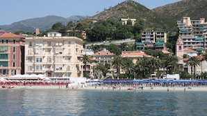 A coastal cityscape with buildings, a beach, and mountains in the background. - Hotel Miranda (Varazze)