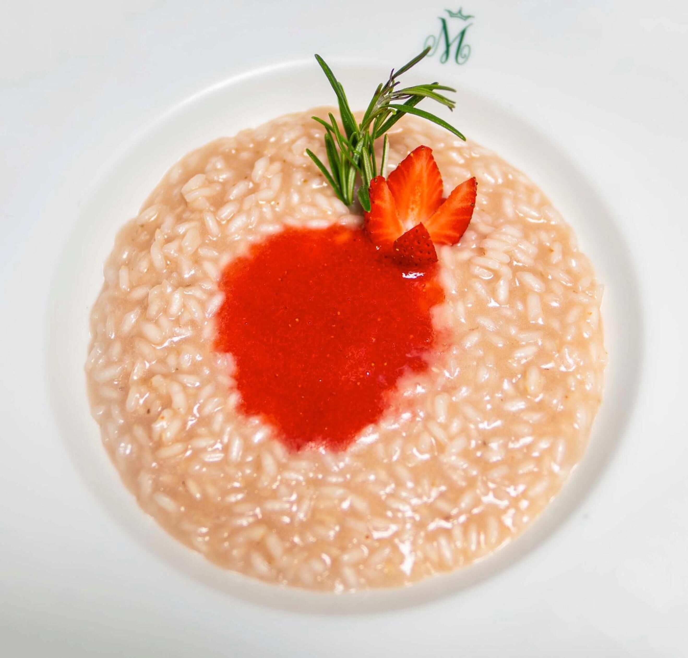 Une assiette de risotto nappé d’une sauce rouge et garnie de fraises.