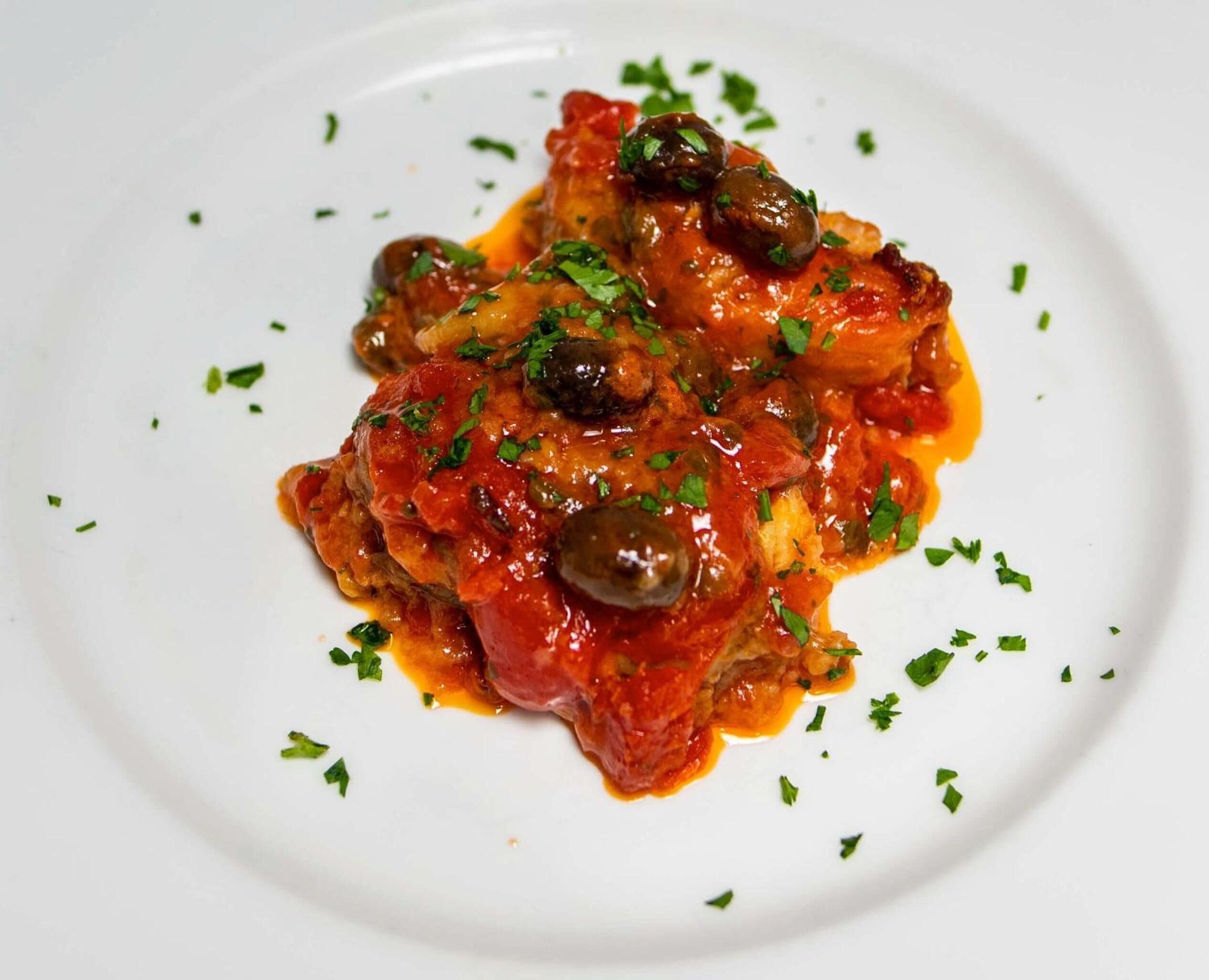 A dish of chicken with olives and tomatoes garnished with herbs.