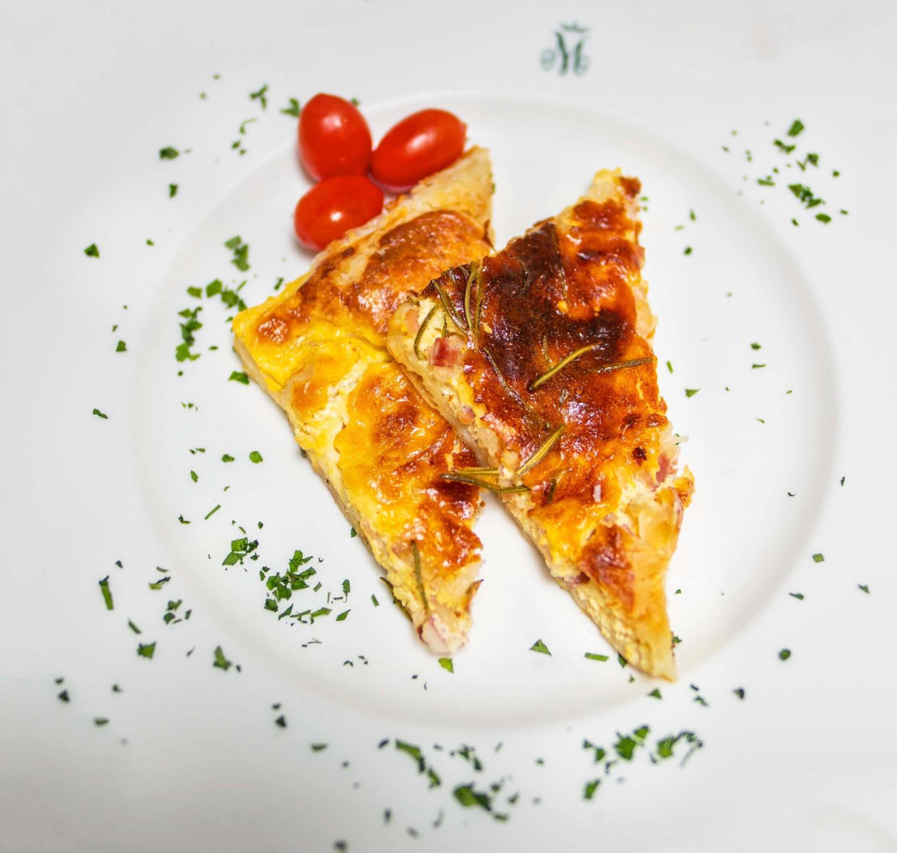 A slice of pizza on a white plate with cherry tomatoes and herbs.