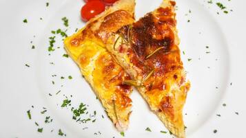 A slice of pizza on a white plate with cherry tomatoes and herbs.
