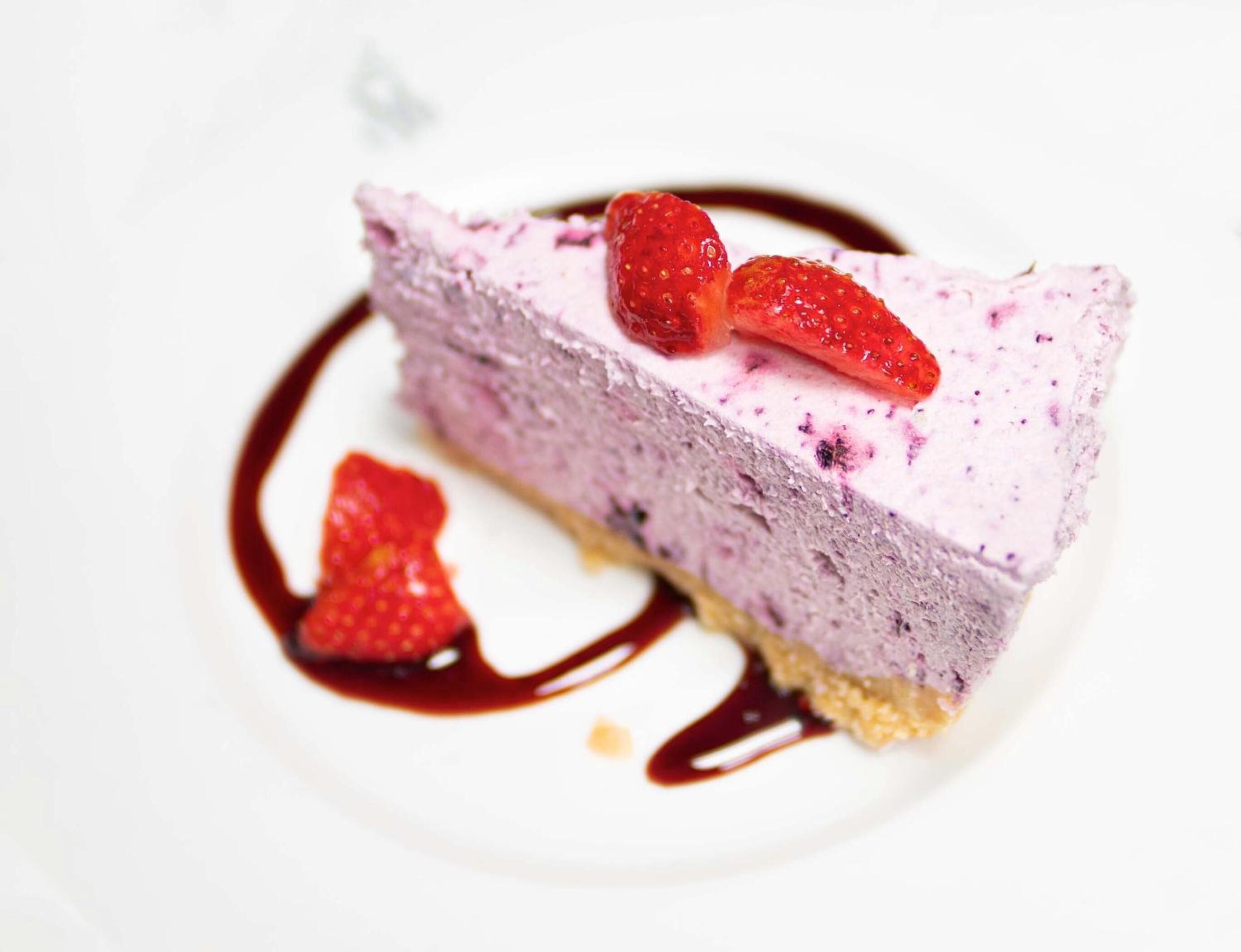 Una porción de pastel de queso con fresas y salsa de chocolate.