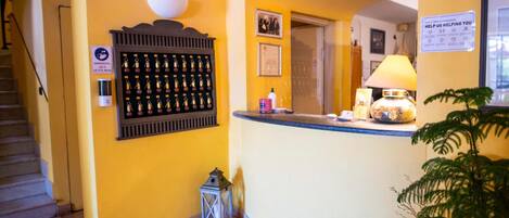 A reception area with a yellow wall, a wall-mounted key display, a small table with a lamp, and a staircase to the left.