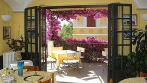 A dining area with open doors leading to a balcony with purple flowers. Tables are set with yellow tablecloths and chairs. - Hotel Miranda (Varazze)