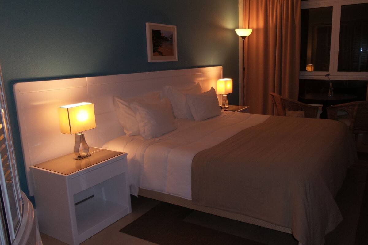 A neatly made bed with two bedside lamps, a small table, and a chair in a hotel room.