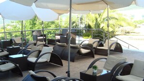 Un patio con mobiliario de mimbre, mesas exteriores y sombrillas que dan sombra.