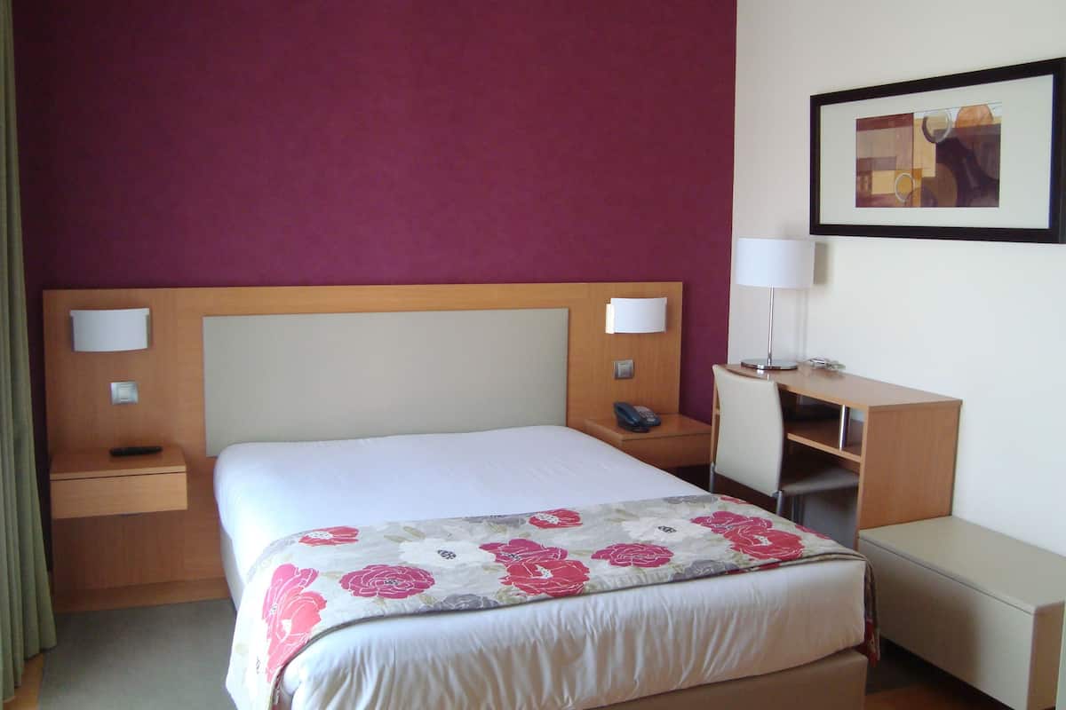 A hotel room with a bed, bedside tables, a desk, and a chair.