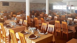 Un amplio comedor con múltiples mesas dispuestas para recibir a los comensales, con sillas y mesas de madera cubiertas con manteles color beige.
