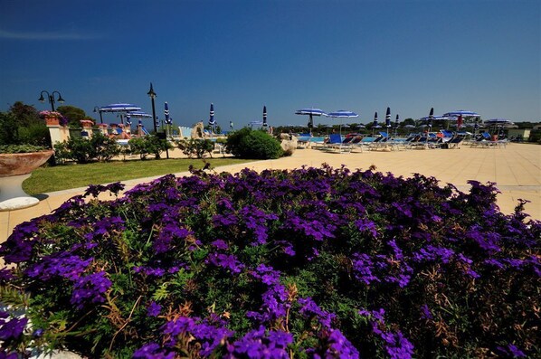 A resort area with a pool, lounge chairs, and a flower garden. - Baia Del Porto (Budoni)