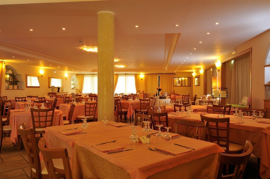 A large dining hall with multiple tables set for a meal, featuring a central column and warm lighting.