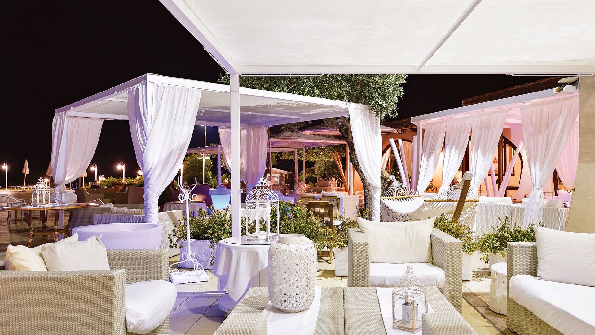 An outdoor patio with white canopies, wicker furniture, and decorative lanterns.