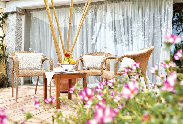A patio with wicker furniture, a table with a fruit bowl, and a view through sheer curtains. - Baia Del Porto (Budoni)