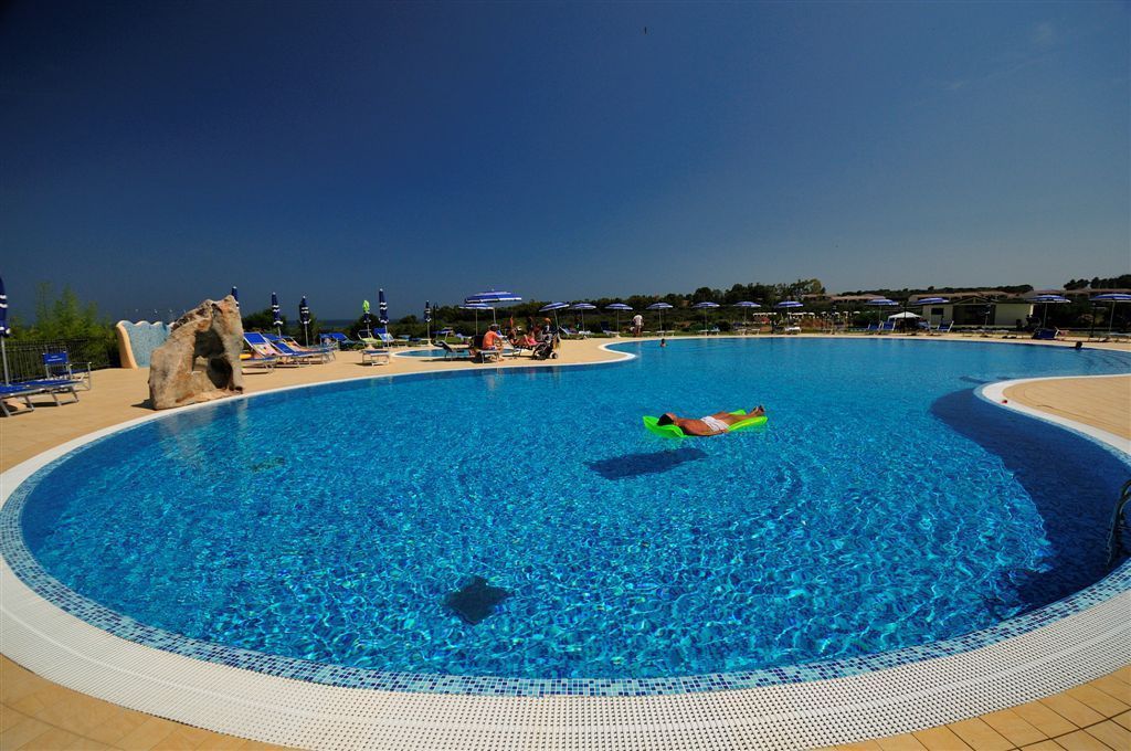 Una grande piscina esterna con acqua cristallina, circondata da lettini e ombrelloni.
