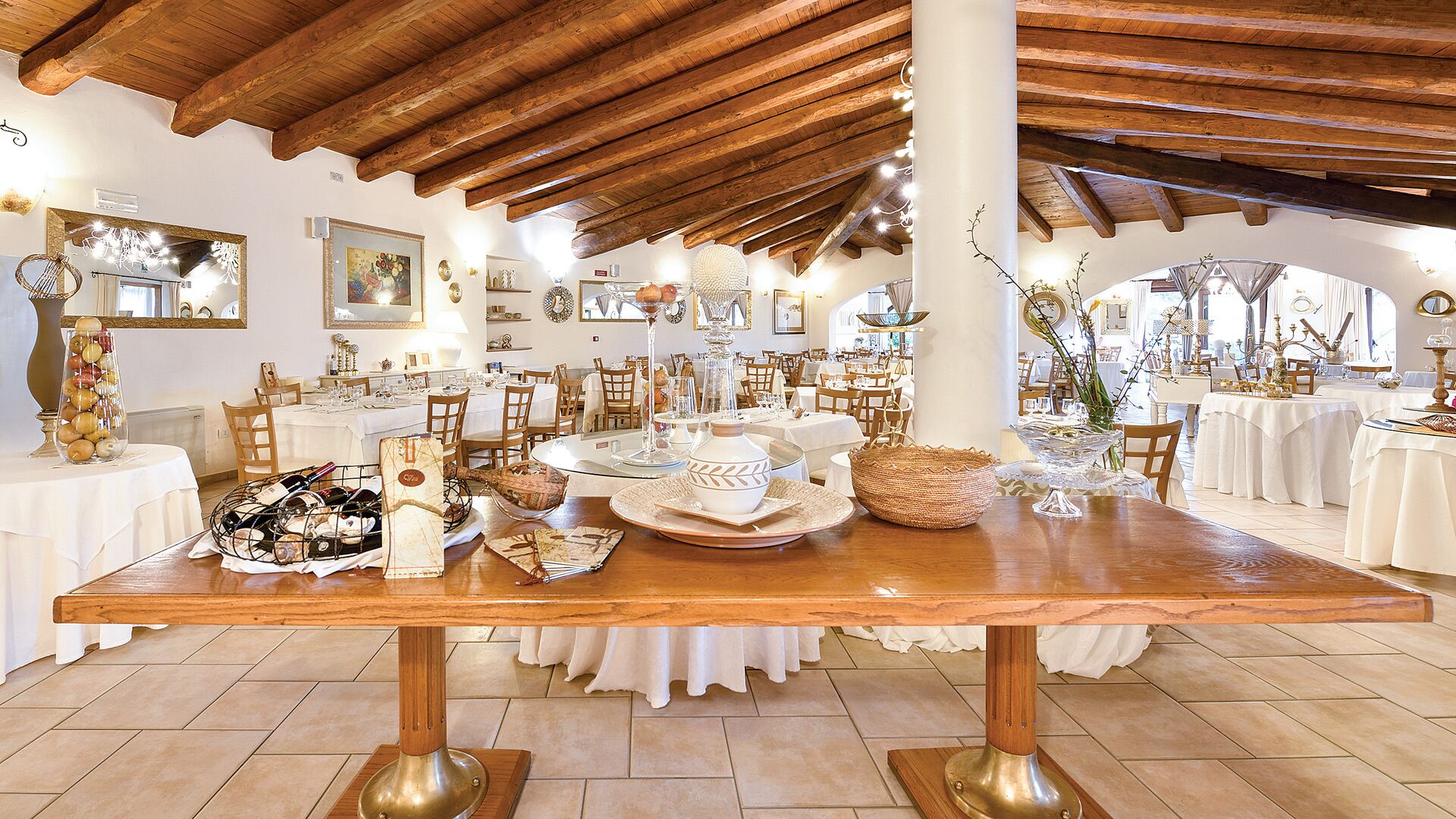 A spacious dining area with a long wooden table, white tablecloths, and various dining ware.
