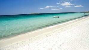 A beach with clear turquoise water, a sandy shore, and a boat in the distance.