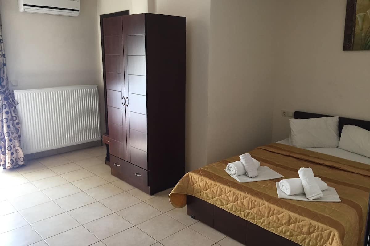 A hotel room with a bed, a wardrobe, a radiator, and an air conditioning unit.