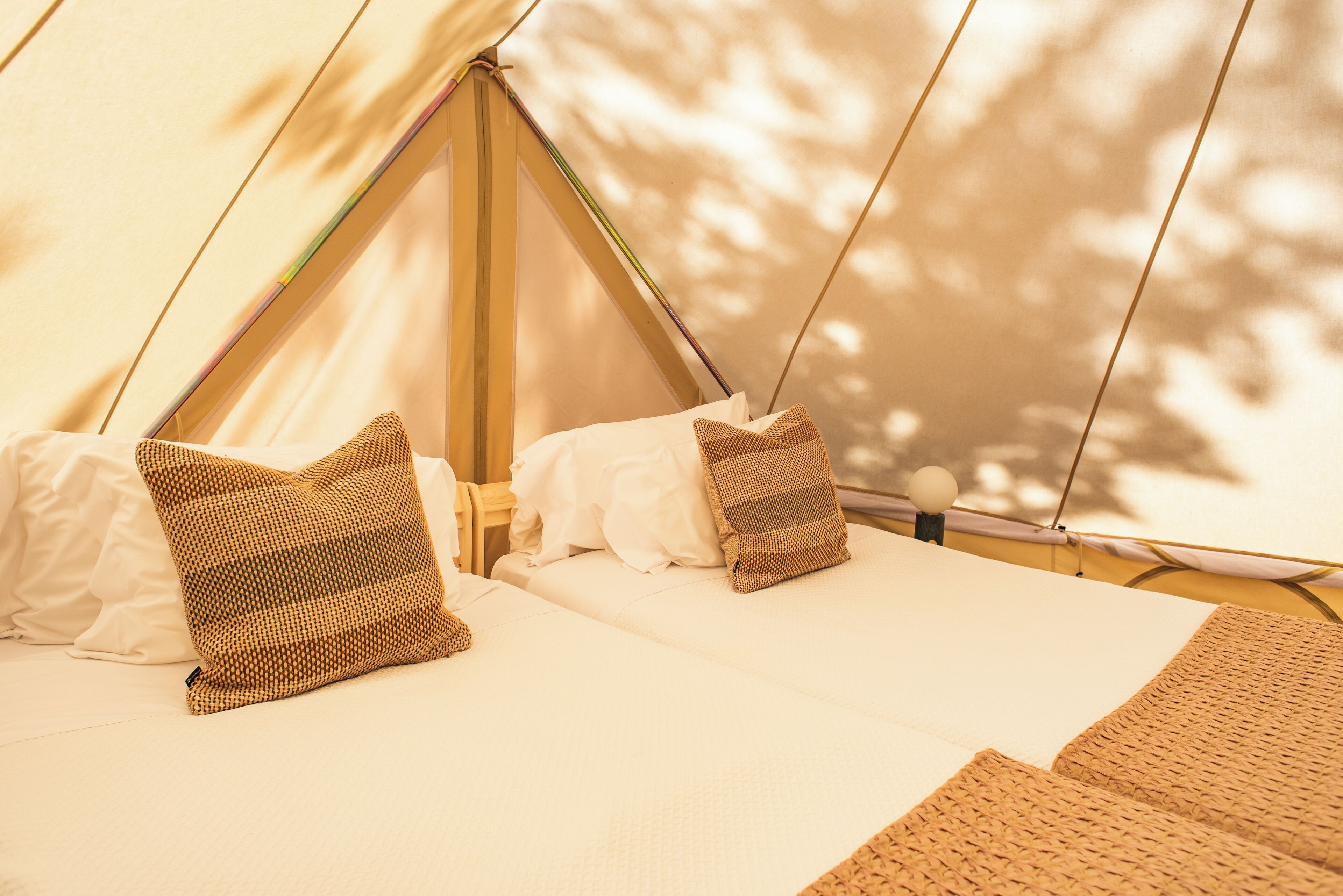 Uma tenda com duas camas, cada uma com roupa de cama branca e almofadas estampadas.
