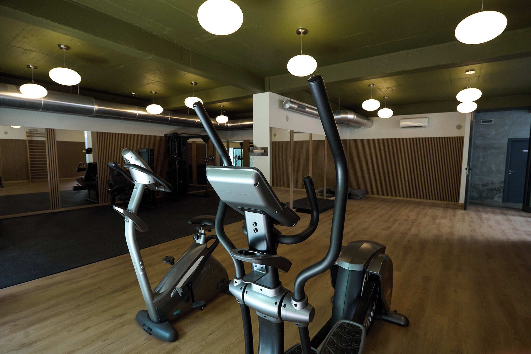 A gym with exercise equipment, mirrored walls, and wooden flooring.