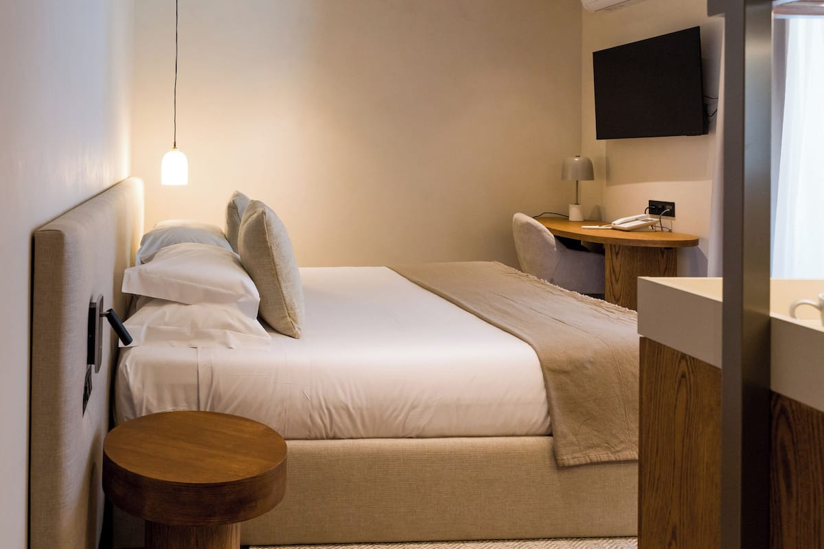 Ein Hotelzimmer mit Bett, Nachttisch, Lampe und einem angebrachten Fernseher.
