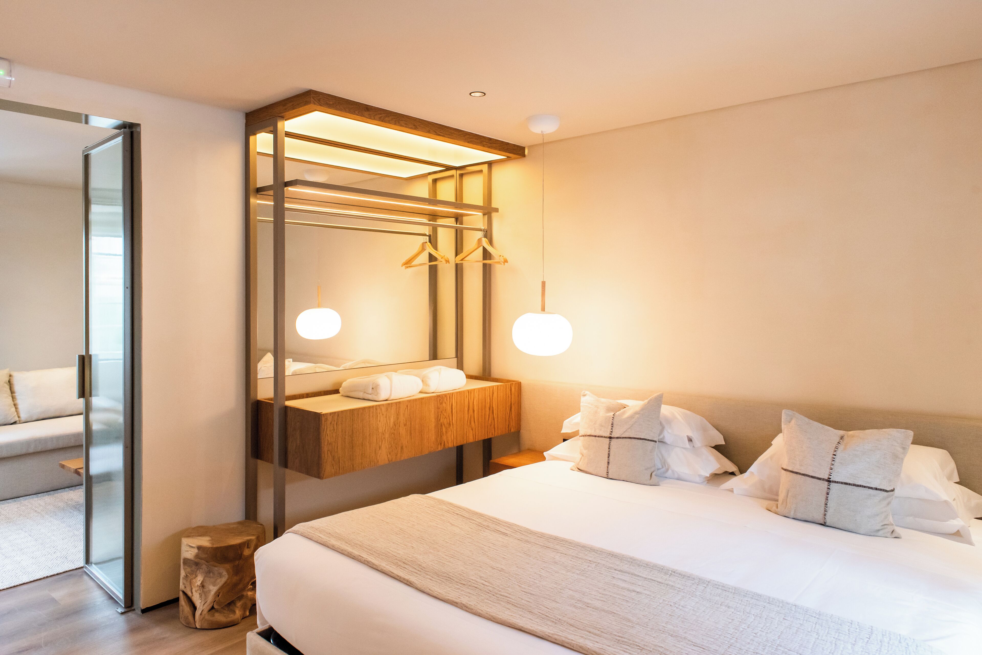 Ein modernes Hotelzimmer mit einem großen Bett, einem Nachttisch aus Holz, einem Spiegel und einer Pendelleuchte.