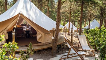 Un campamento boscoso con una tienda de campaña grande, una silla de descanso y un camino de piedra.