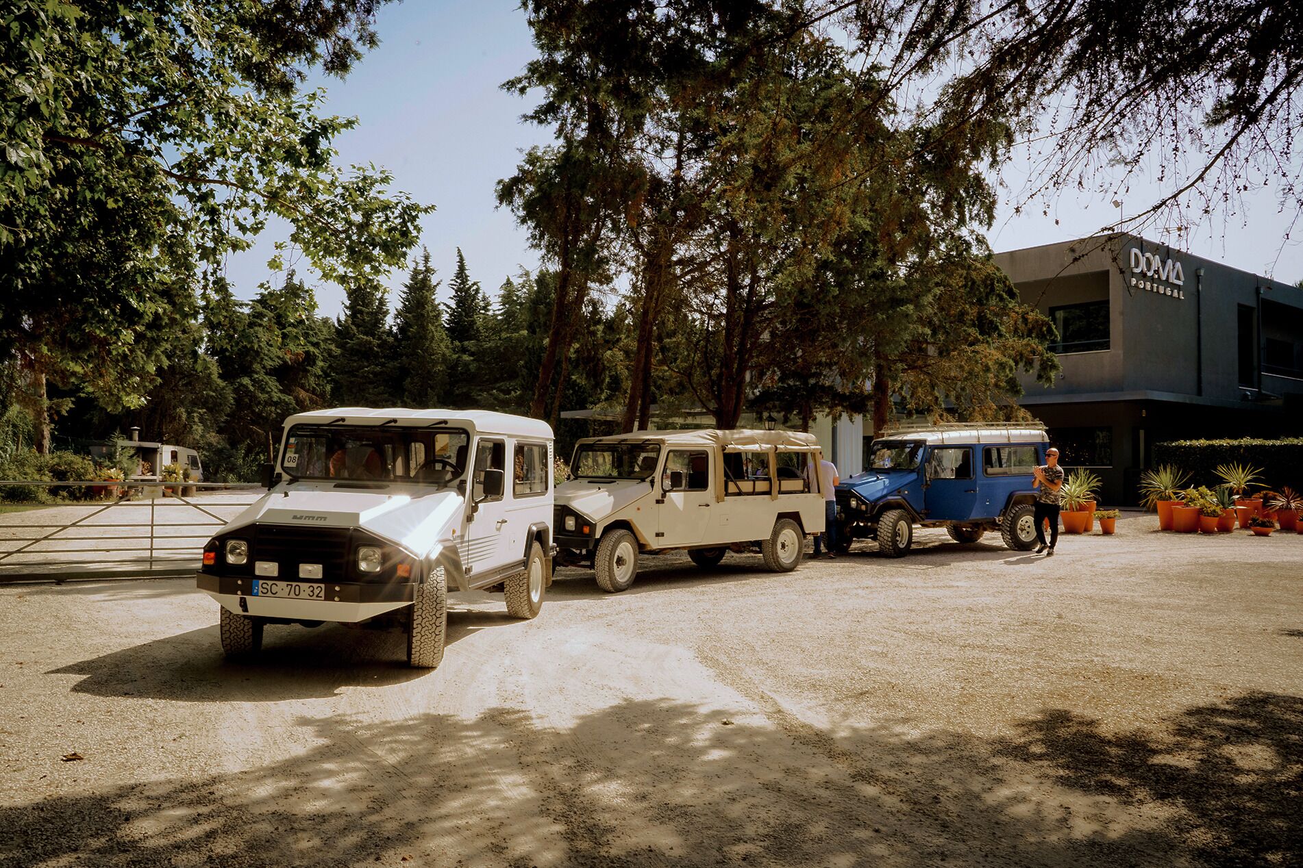 Two off-road vehicles parked in a gravel area with trees and a building labeled 'DOMA PORTAL' in the background.