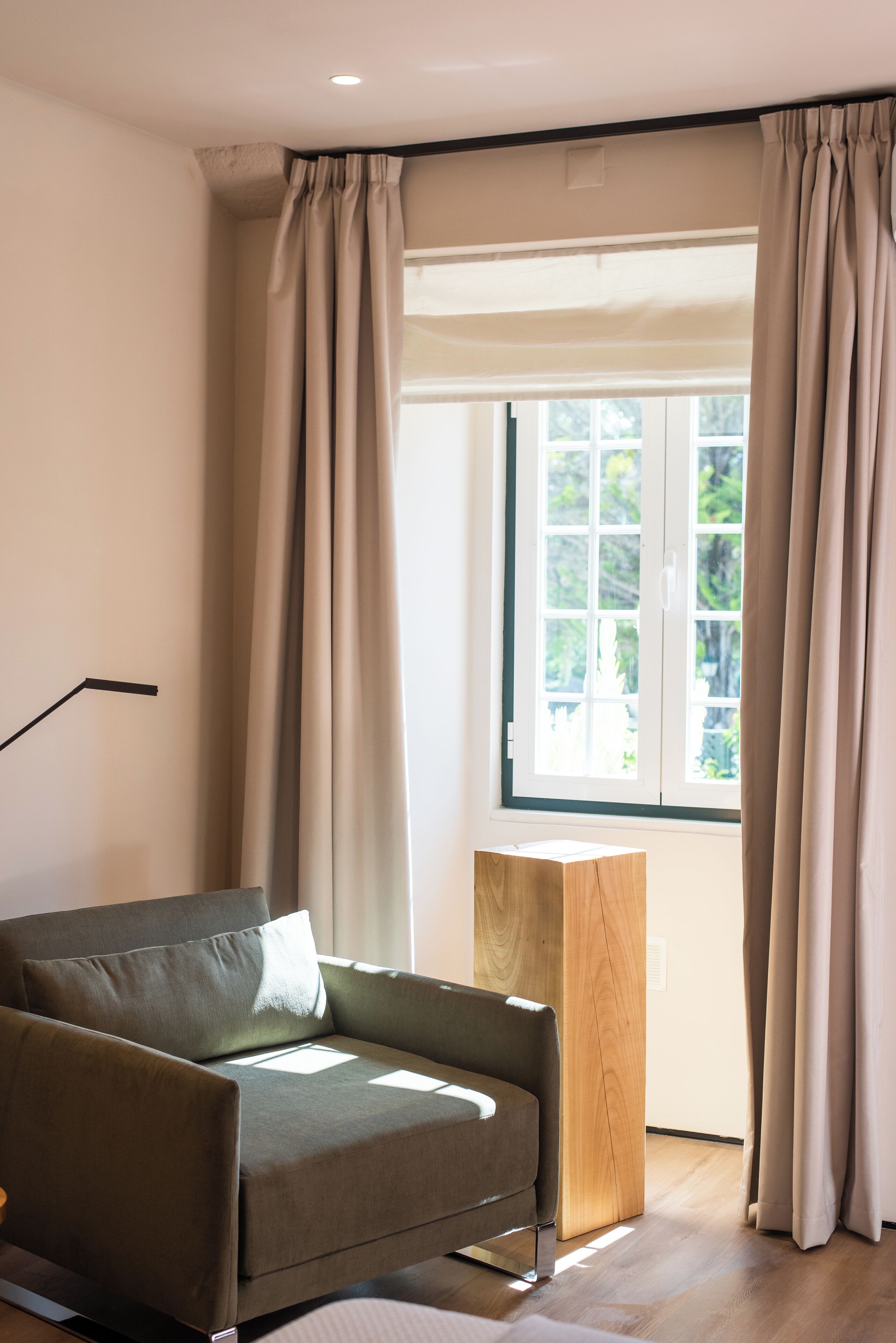Een moderne woonkamer met een bank, een houten bijzettafeltje en een groot raam met gordijnen.