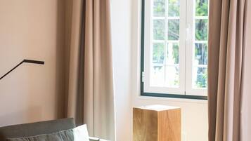 A modern living room with a sofa, a wooden side table, and a large window with curtains.