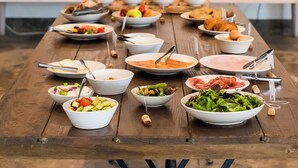 Una larga mesa de madera con diversos platos y tazones de comida, una máquina de café y una ventana al fondo.