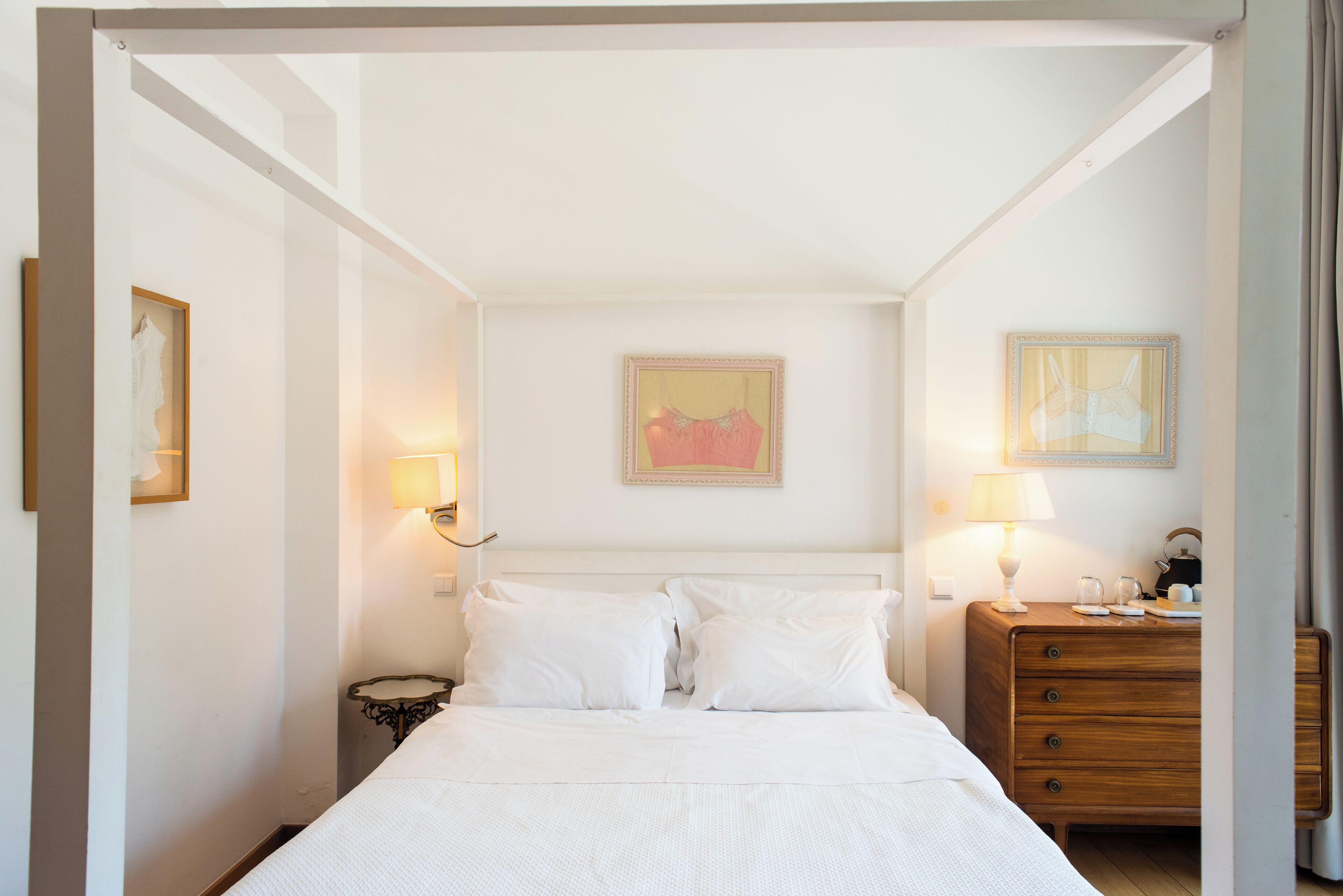 Una habitación de hotel con una cama, lámparas de noche, un aparador y dos cuadros en la pared.