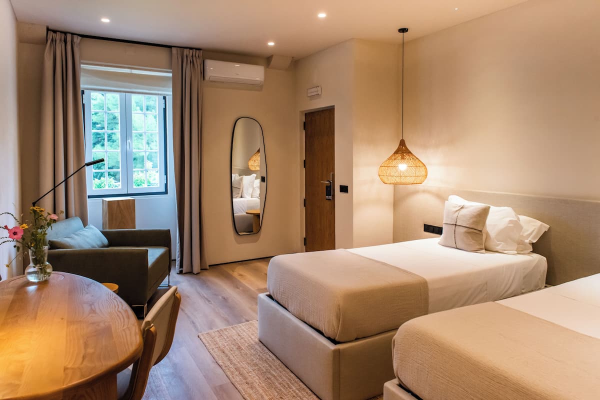 Ein Hotelzimmer mit einem Holztisch, einer Couch, zwei Betten, einem Spiegel und einer Hängelampe.