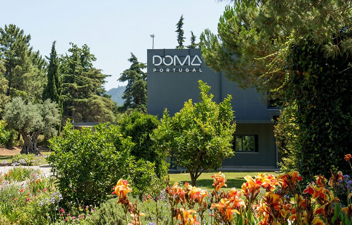 Un edificio moderno con un letrero que dice 'DOMA PORTUGAL', rodeado de exuberante follaje y plantas en flor.