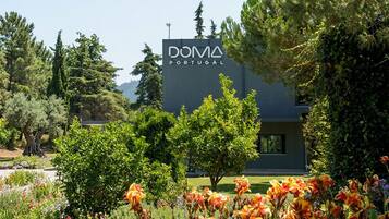Un edificio moderno con un letrero que dice 'DOMA PORTUGAL', rodeado de exuberante follaje y plantas en flor.