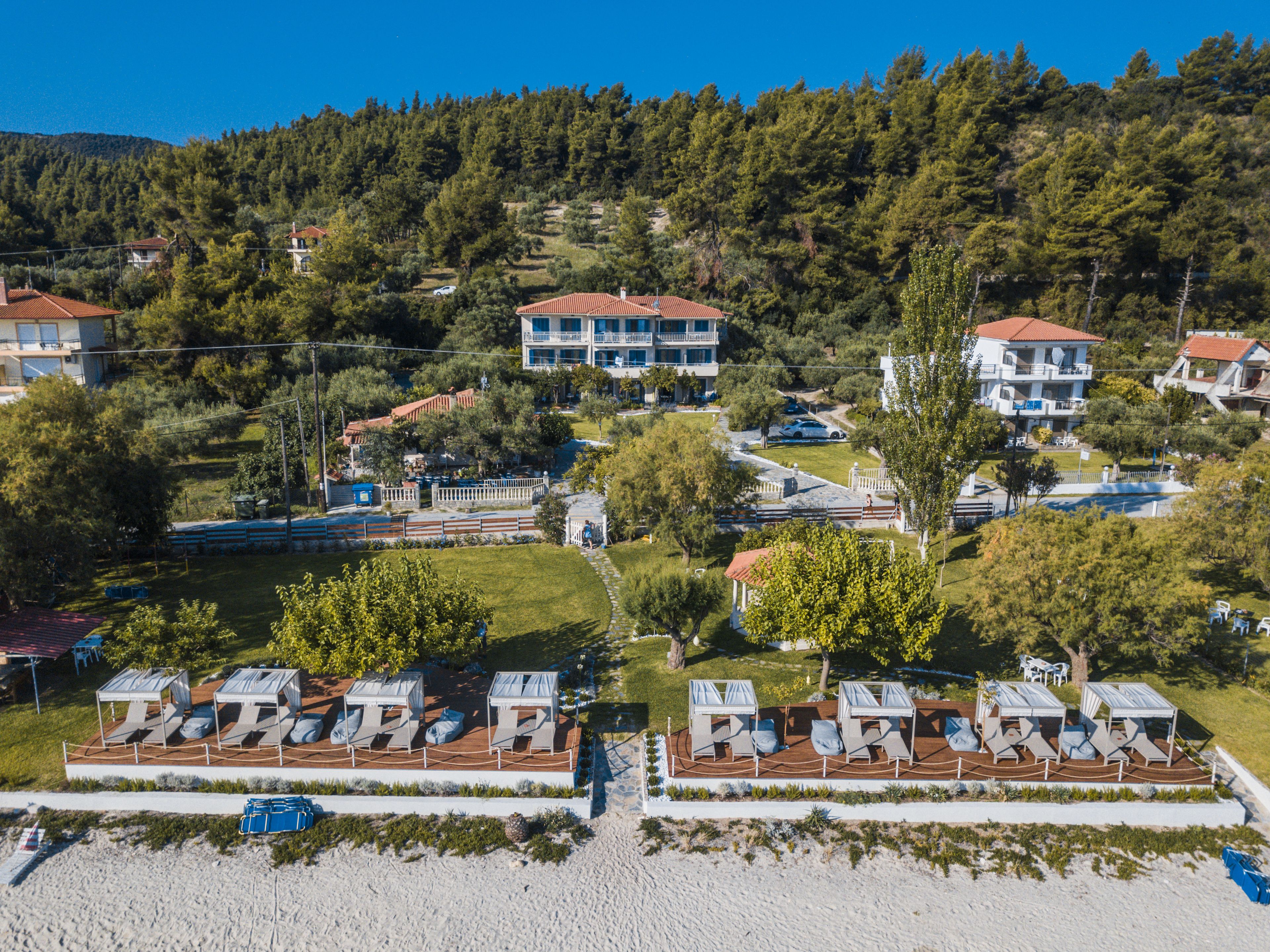 A coastal resort with multiple villas, a beach area with sun loungers, and a forested hillside in the background.